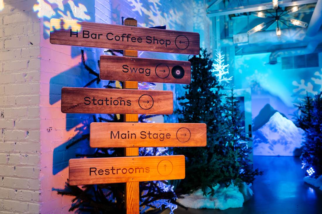Wood-look wayfinding signpost with directions to stations, swag, and main stage