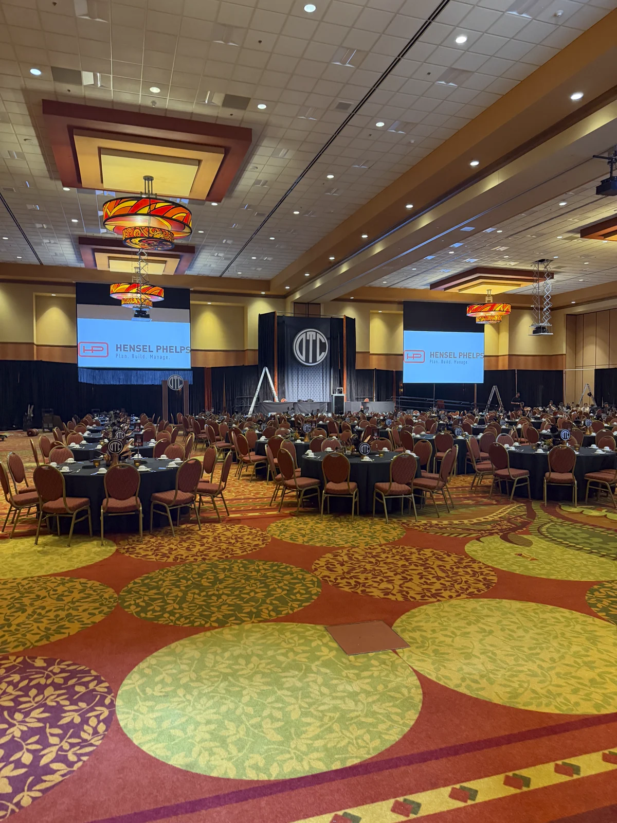 The ballroom filled with guests, the lit monogram and screens at the far end