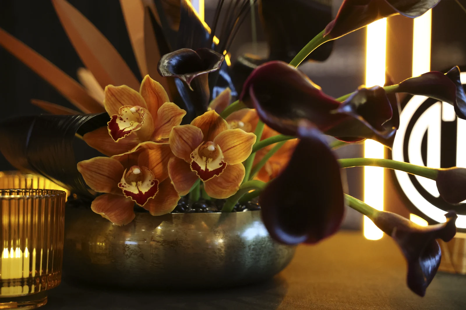 Close detail of amber orchids and calla lilies with the illuminated OTC mark behind