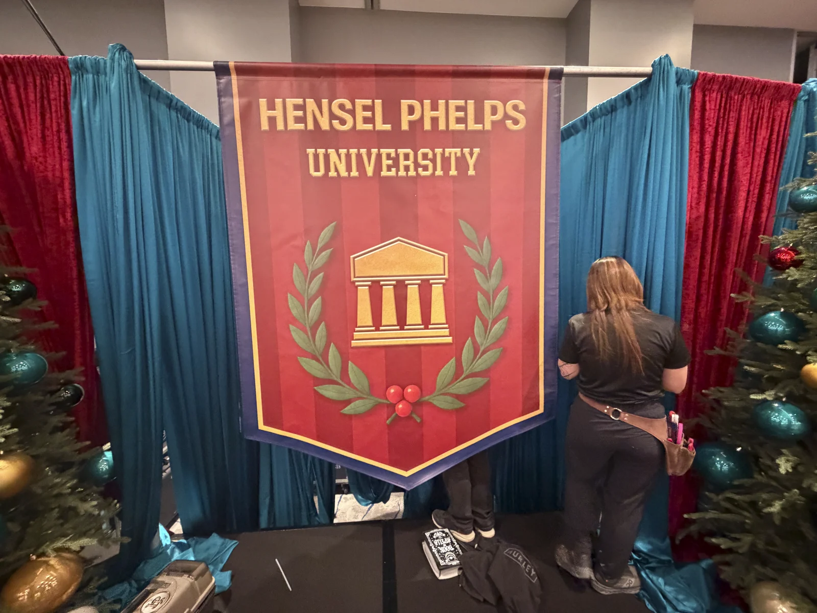 Hensel Phelps University crest banner being hung against red and teal drapery
