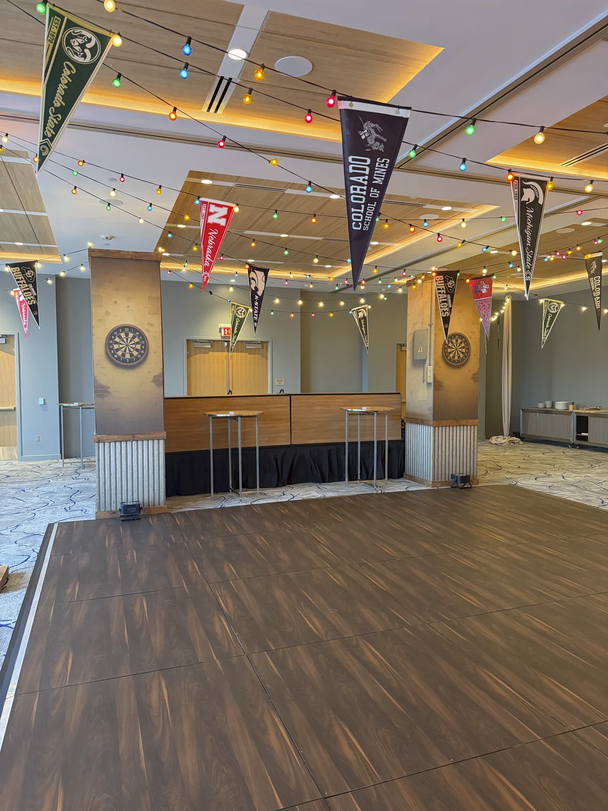 Dive bar room with dartboard pillar graphics and college pennants strung overhead