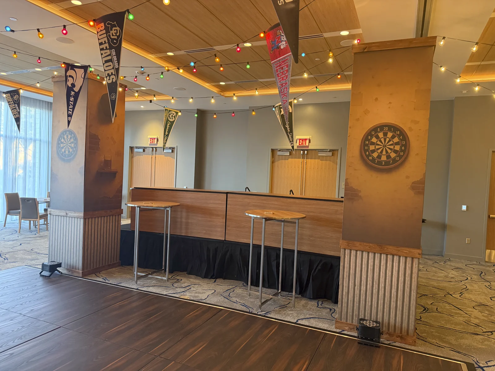 Bar pillars wrapped in weathered brick and plaster vinyls with a painted dartboard, under strung pennant flags