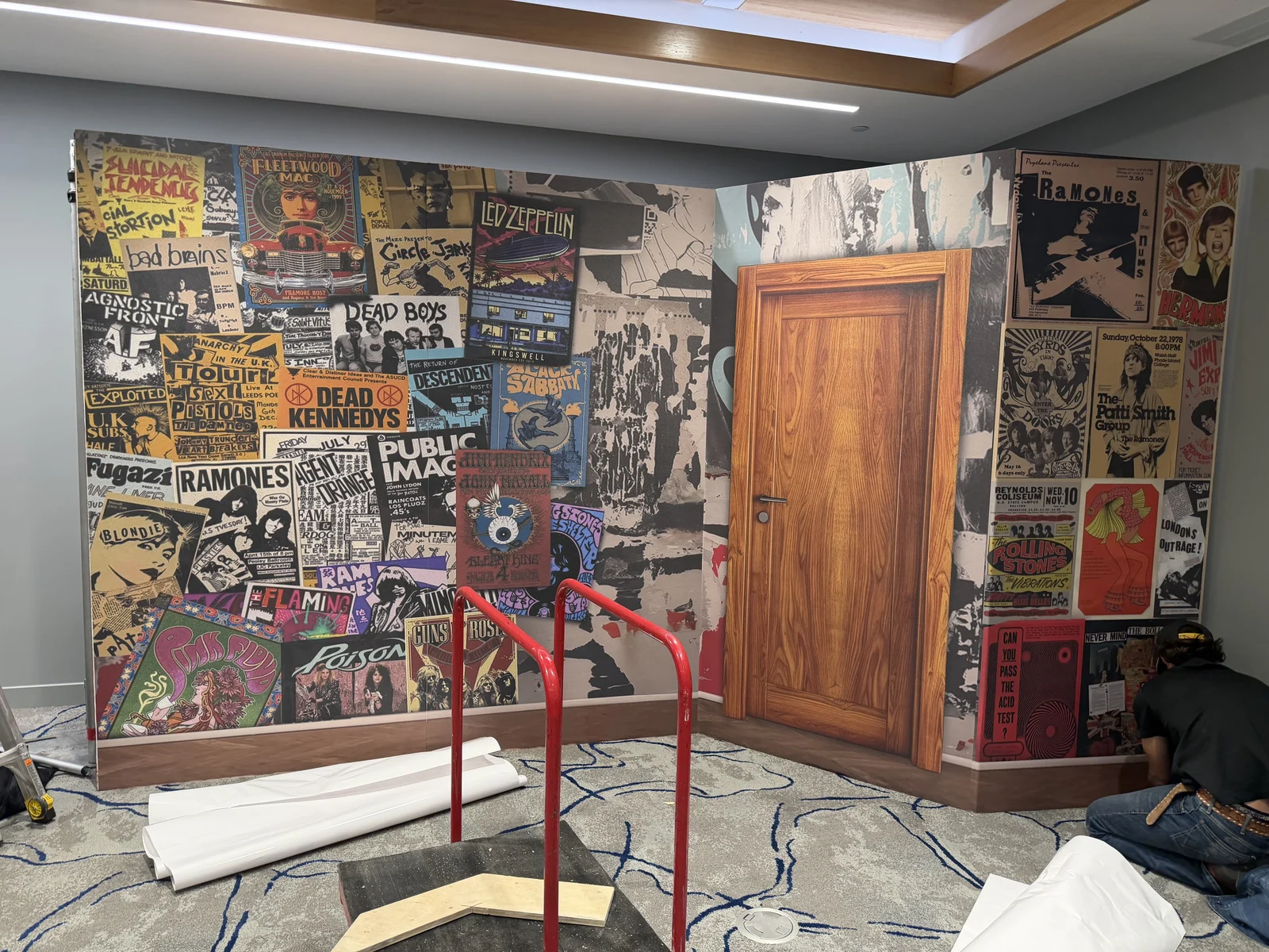 The printed poster-wall panels standing on site mid-install, with the printed dorm door