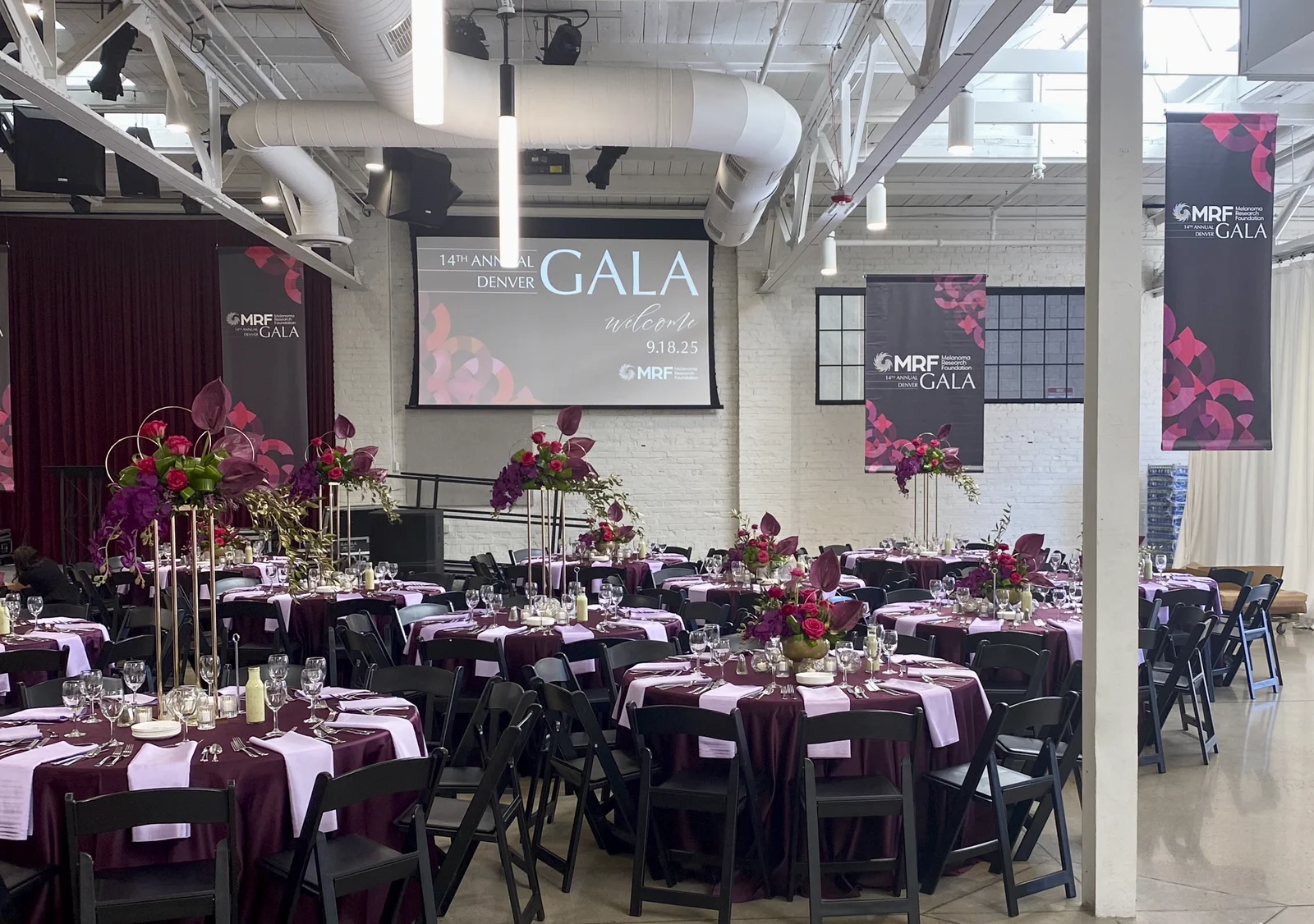 Ballroom set for dinner with MRF Denver Gala banners and the welcome screen graphic