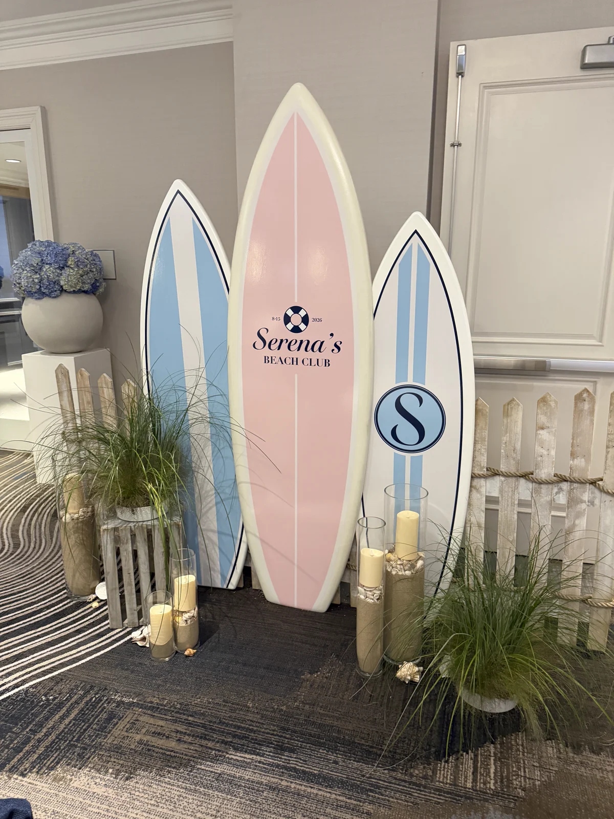 Three branded surfboards styled with candles, grasses, and a picket fence